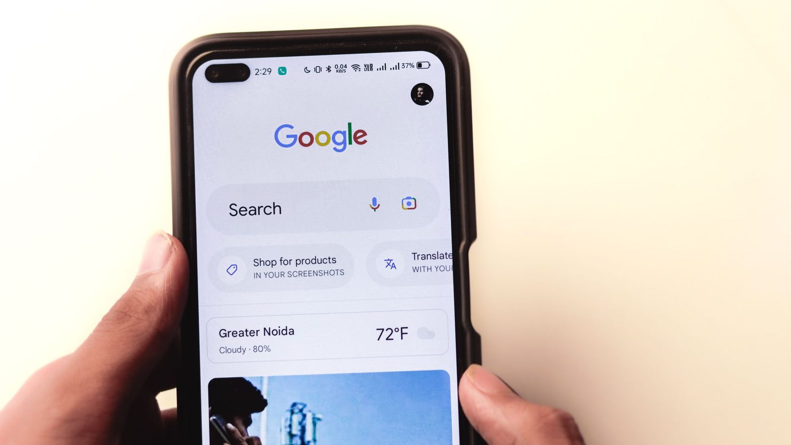 A hand holding a smartphone open to the Google Search home screen.